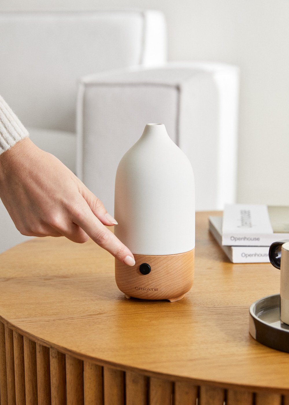 Una mano presiona un botón en un difusor blanco y de madera sobre una mesa de madera.