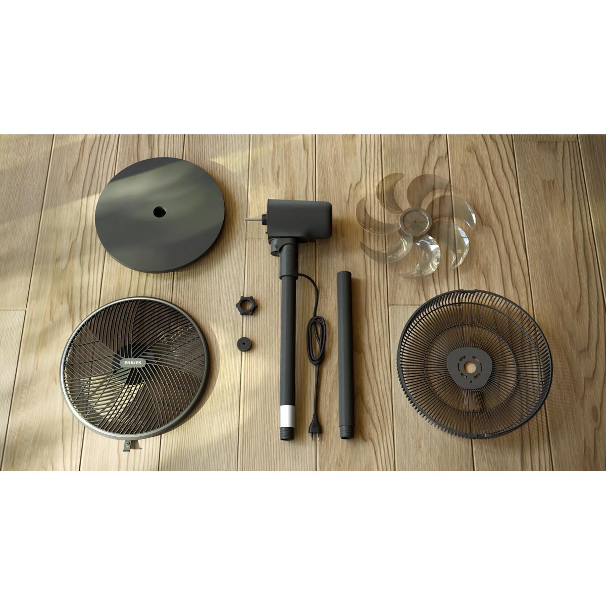 Pièces de ventilateur sur plancher en bois : socle, grille, moteur, pales et mât.