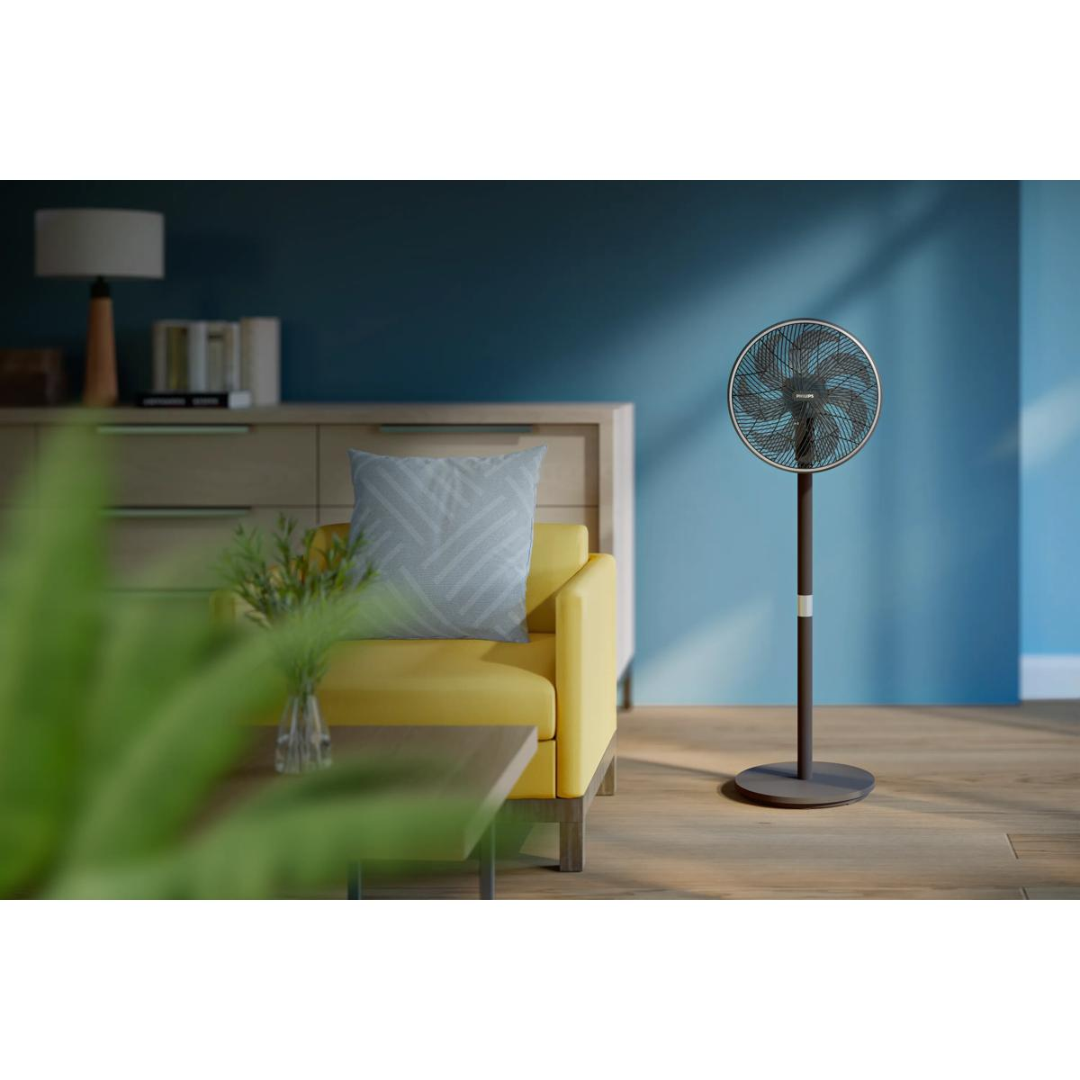 Un ventilateur sur pied est à côté d'un canapé jaune avec un coussin, devant un buffet.