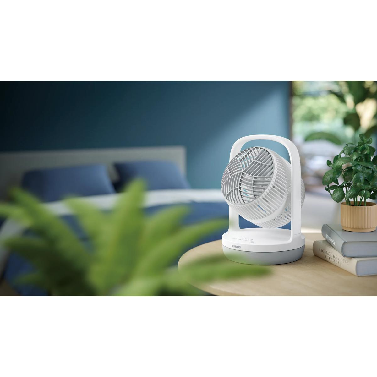 Weißer Ventilator auf einem Nachttisch in einem Schlafzimmer mit blauem Bett.