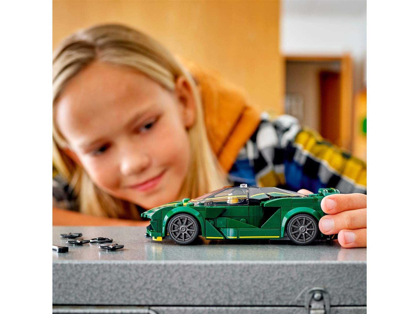 Ein Mädchen betrachtet ein grünes Lego-Auto auf einer grauen Oberfläche mit losen Teilen.