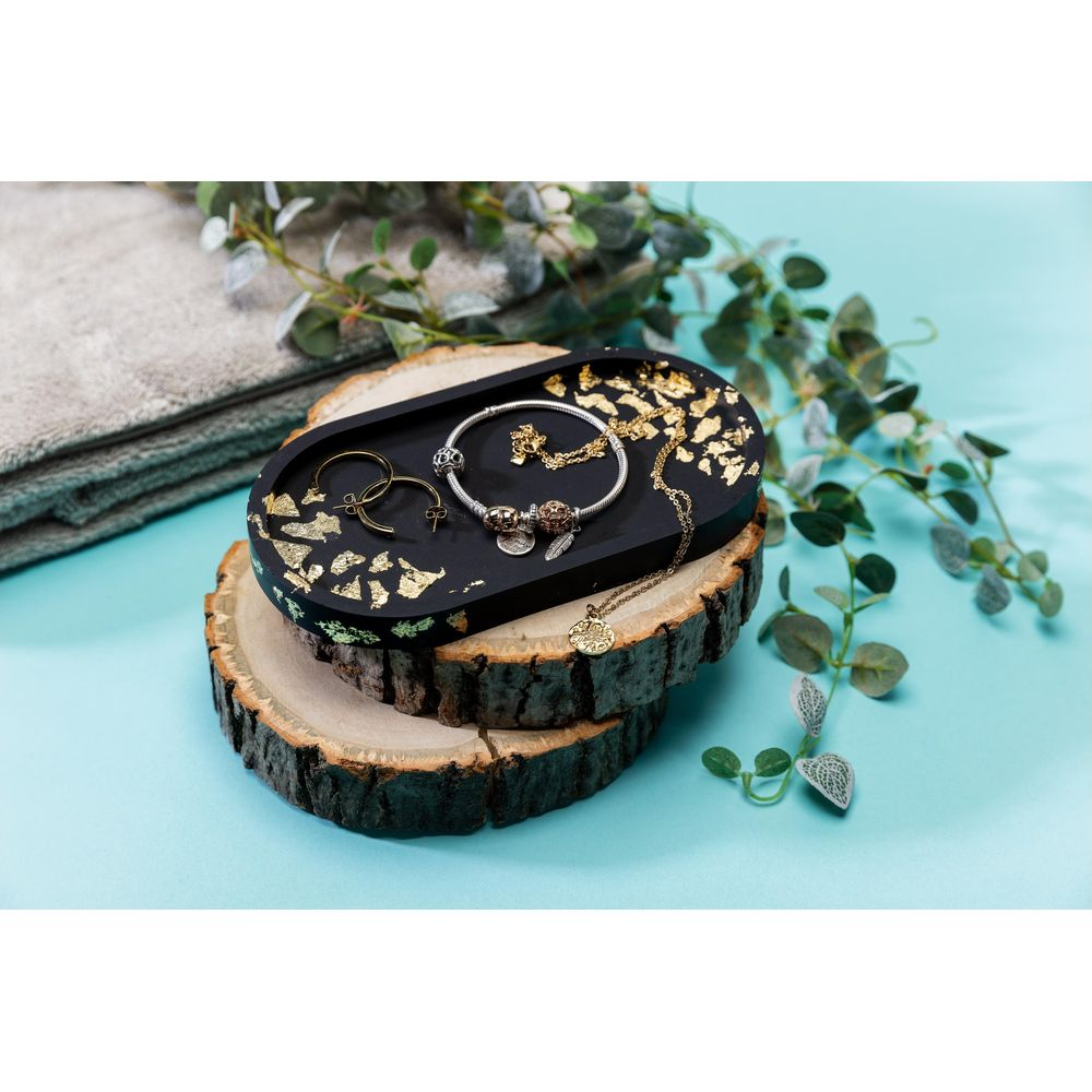 Schwarze Schmuckschale mit Goldfolie auf Holzscheiben, daneben ein Handtuch.