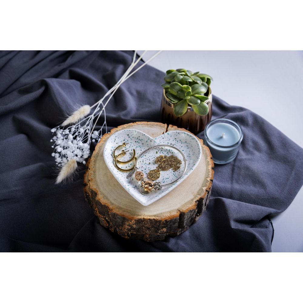 Piatto portagioie a forma di cuore con orecchini e collana su fetta di legno.