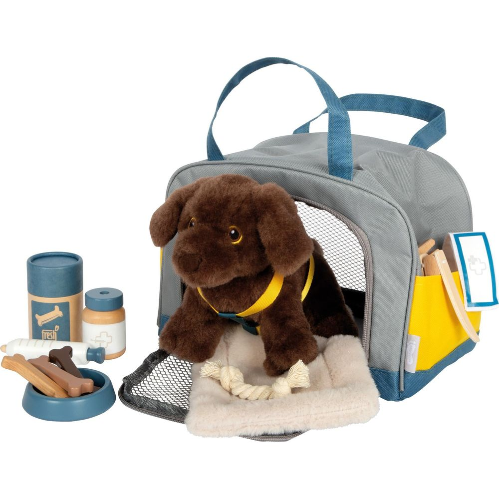 Chien en peluche marron dans une cage de transport grise avec des accessoires à côté.
