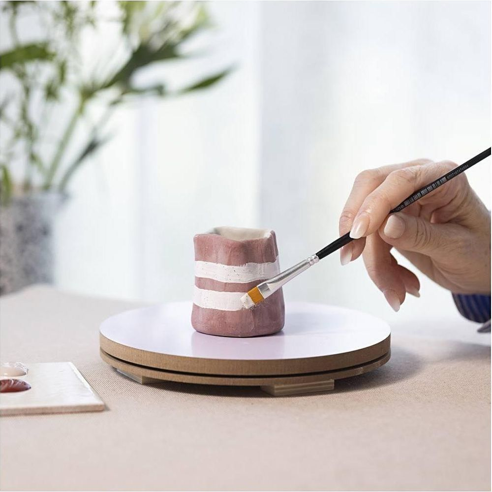 Una mano dipinge strisce bianche su un vaso di ceramica rosa su un piatto girevole.