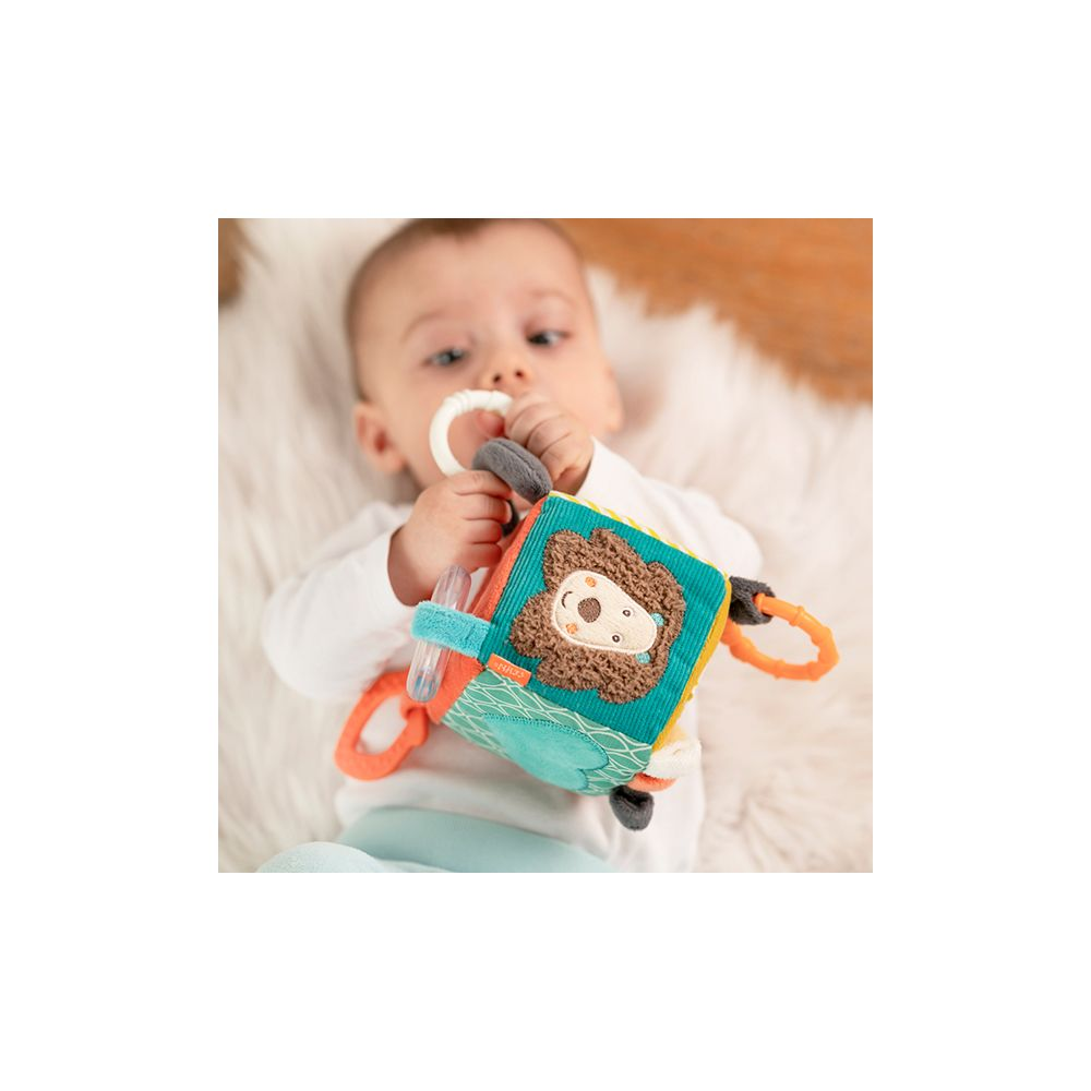Bébé allongé sur un tapis moelleux, jouant avec un livre en tissu coloré à motif lion.