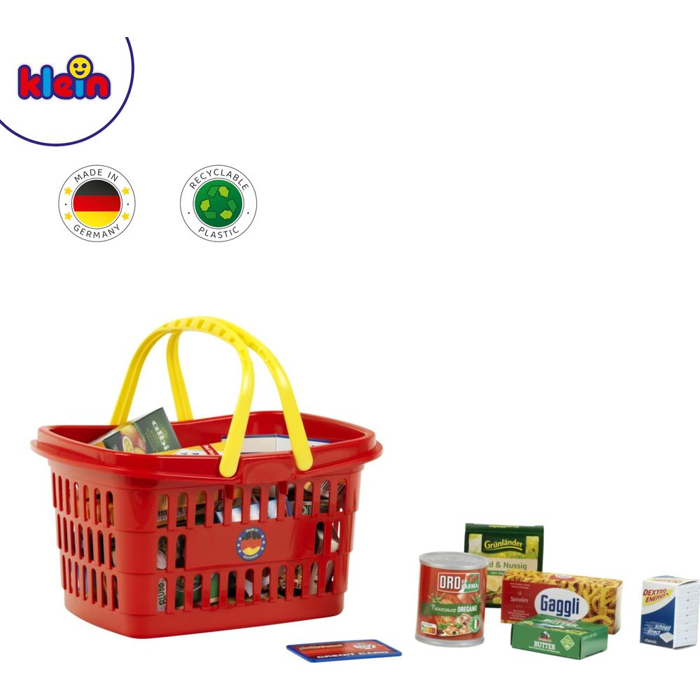 Un panier de courses en plastique rouge avec poignées jaunes, rempli de jouets alimentaires. Comprend de petites boîtes et une conserve.