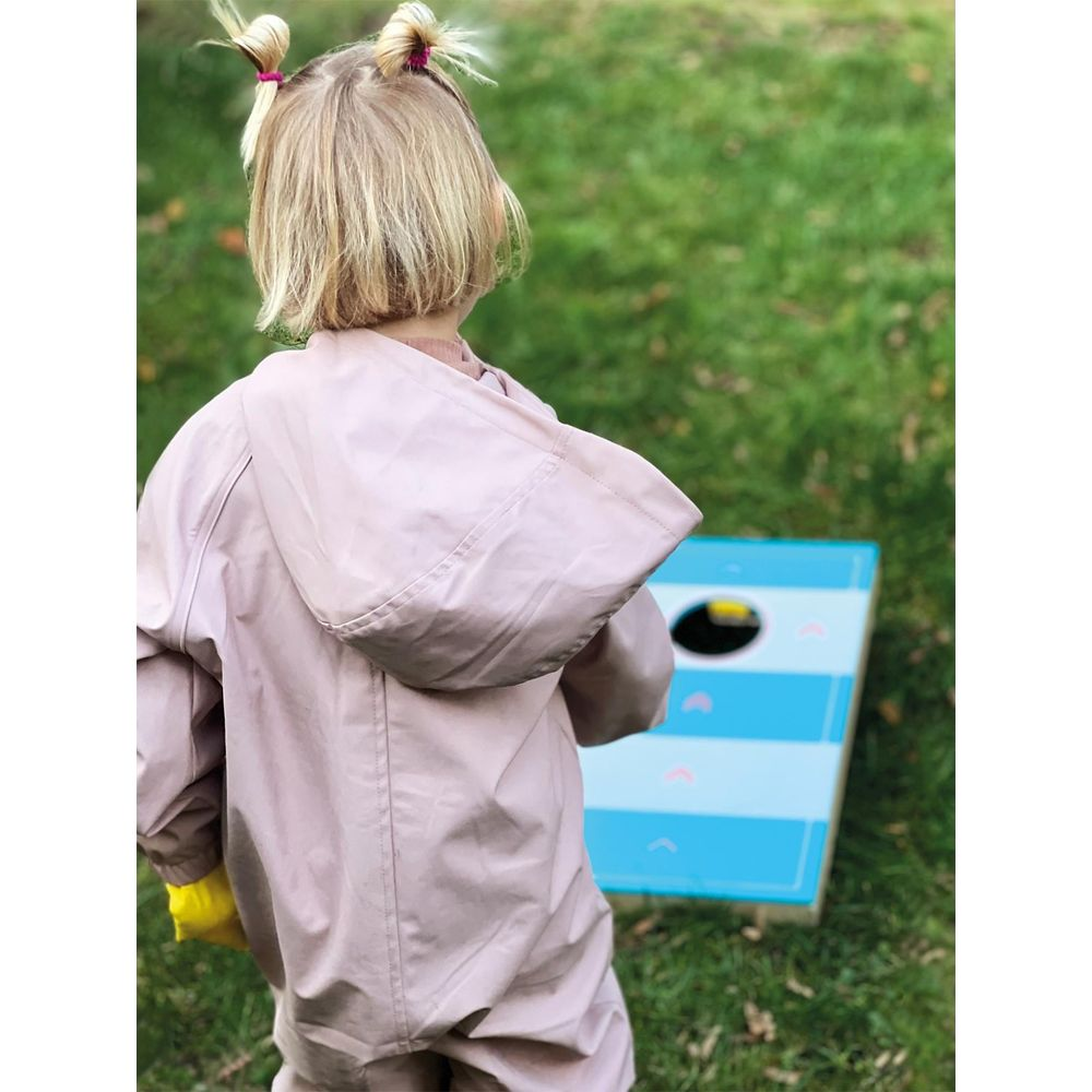 Una bambina con un cappotto rosa con cappuccio gioca a cornhole su un prato.