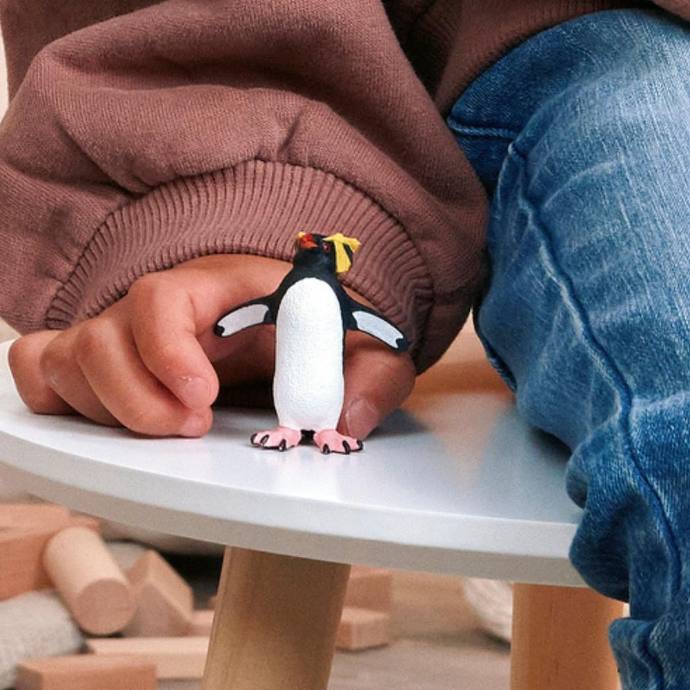 Un niño sostiene una pequeña figura de pingüino sobre una mesa blanca.
