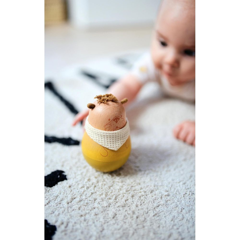 Un bébé est allongé sur un tapis jouant avec un jouet lion en bois.