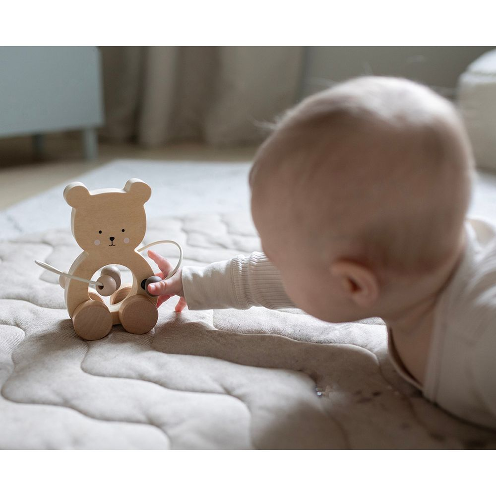 Ein Baby spielt mit einem hölzernen Bärenspielzeug auf einer weichen Matte.