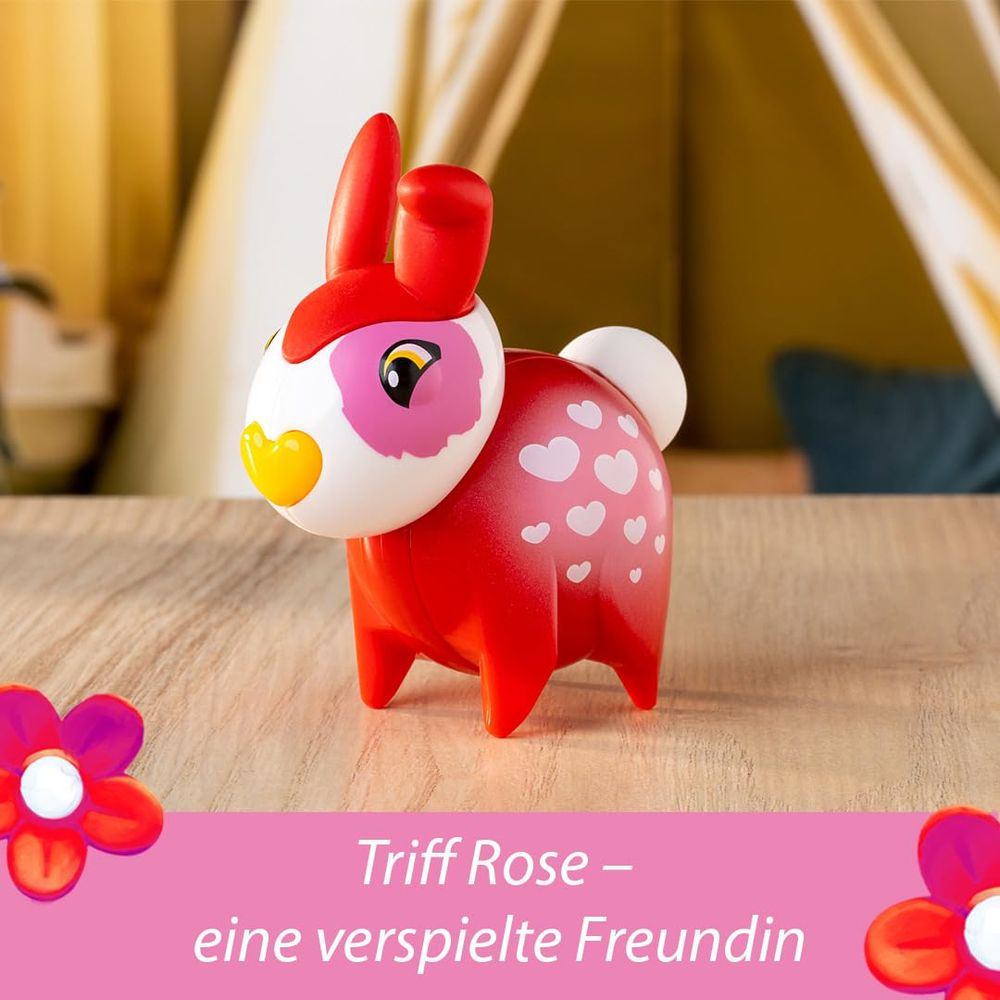 Un lapin jouet rouge avec des cœurs roses est assis sur une table en bois. Deux fleurs roses au premier plan.