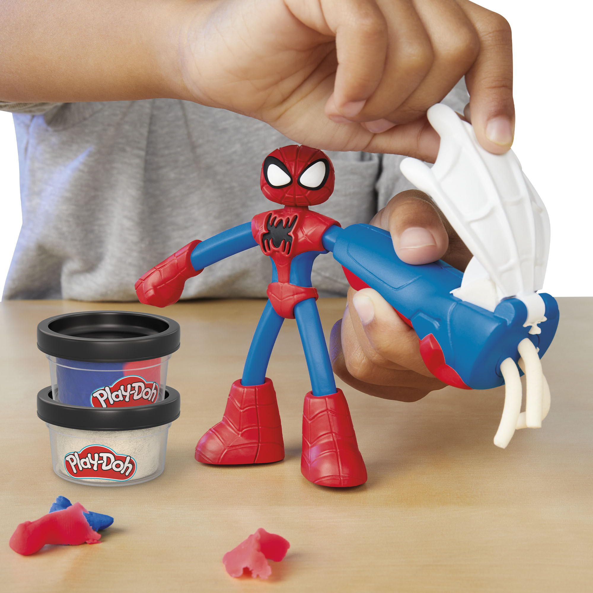 Dziecko używa niebiesko-czerwonego narzędzia Play-Doh do wyciskania białych pasm na figurkę Spidermana.