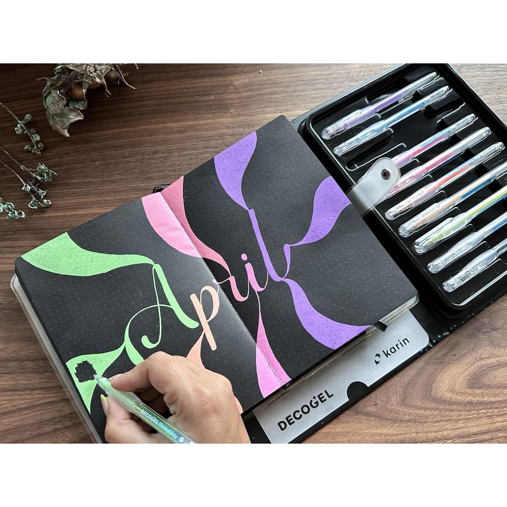Eine Hand malt mit einem grünen Stift auf ein Notizbuch mit der Aufschrift „April“.