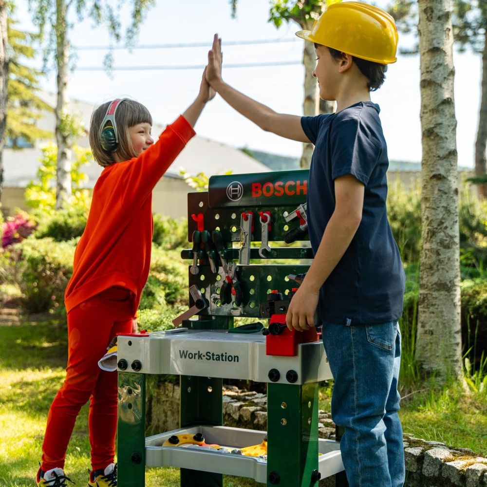Dwoje dzieci daje sobie piątkę na zewnątrz przed stołem warsztatowym Bosch.
