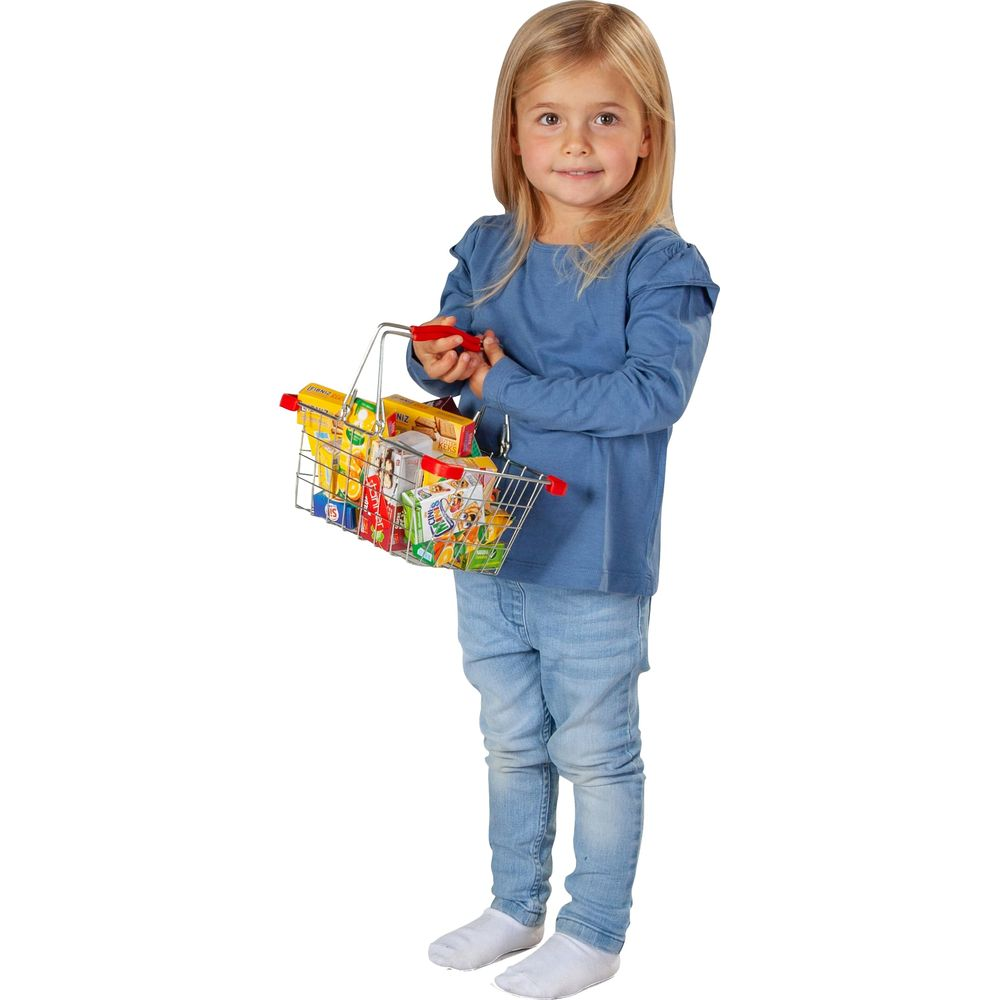 Ein junges Mädchen im blauen Hemd und Jeans hält einen Einkaufskorb voller Spielzeug-Lebensmittel.