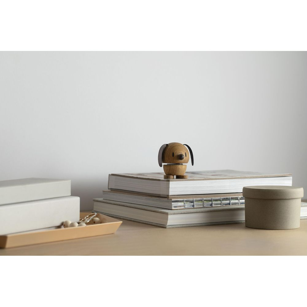 Un cane di legno seduto su libri accanto a una scatola rotonda.