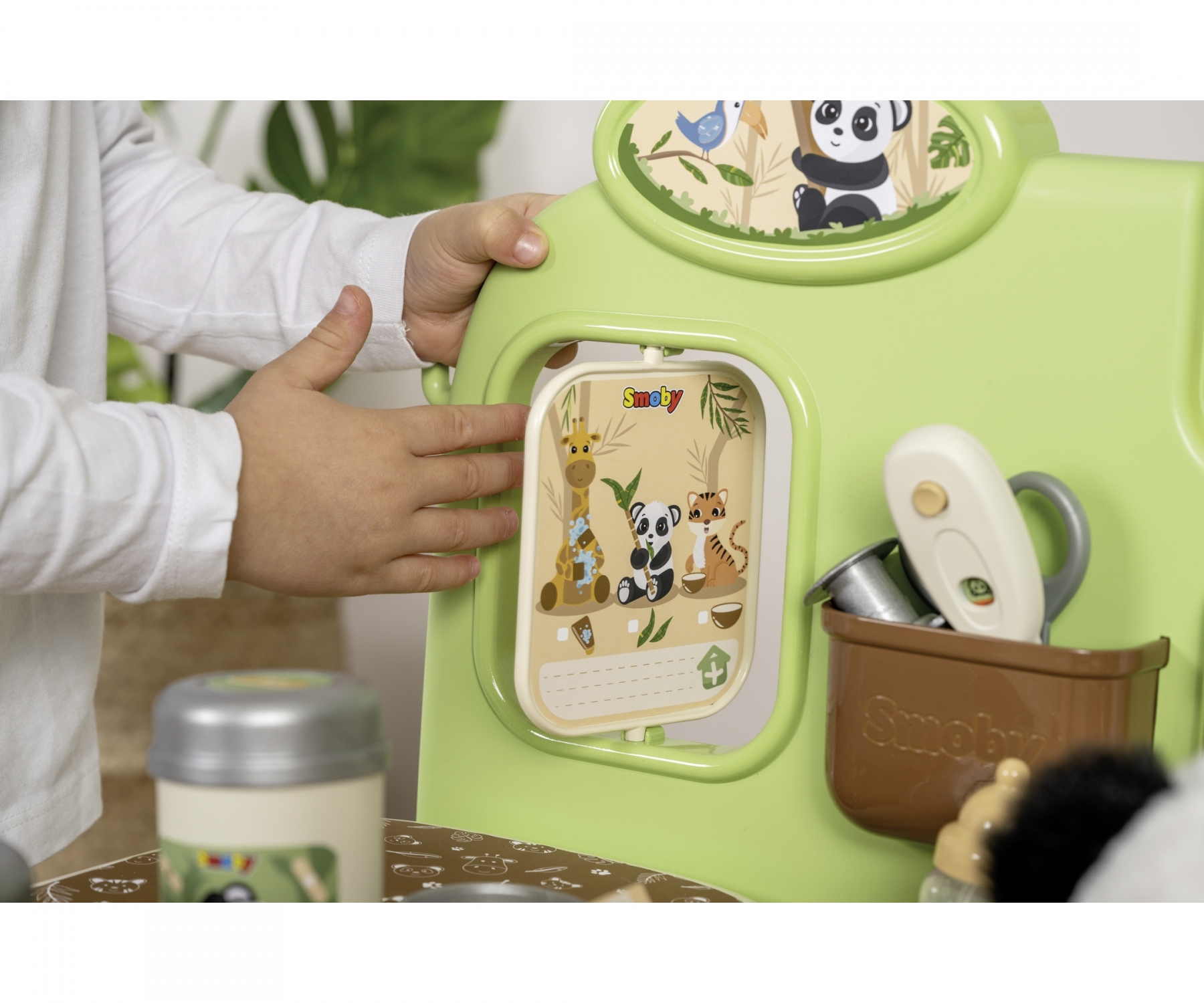 Kinderhände spielen mit einem grünen Smoby-Spielzeug. Ein Panel zeigt Zeichentricktiere: Giraffe, Panda, Tiger.