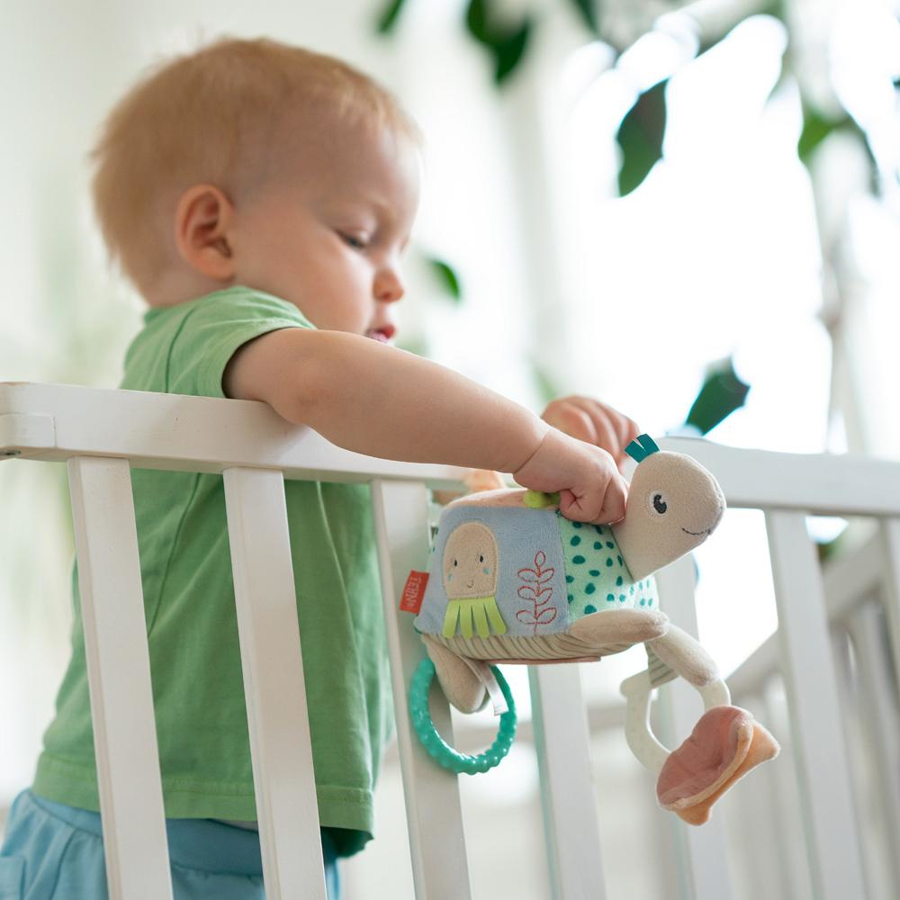 Un bambino con una maglietta verde gioca con un sonaglio a forma di tartaruga in una culla.