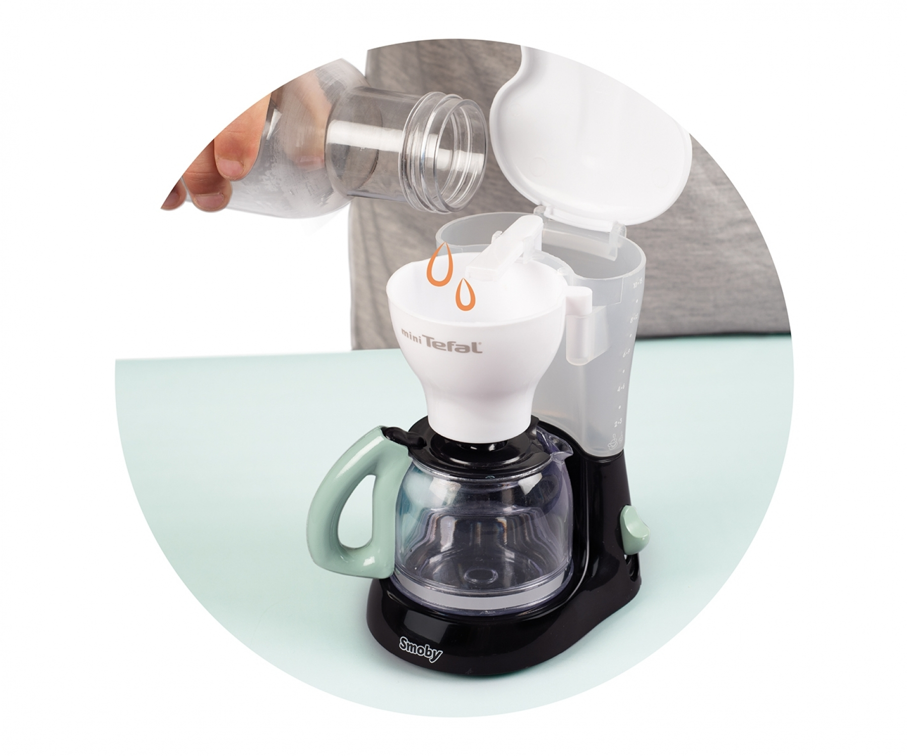 Ein Kind gießt Flüssigkeit aus einer Plastikflasche in eine Spielzeug-Kaffeemaschine.
