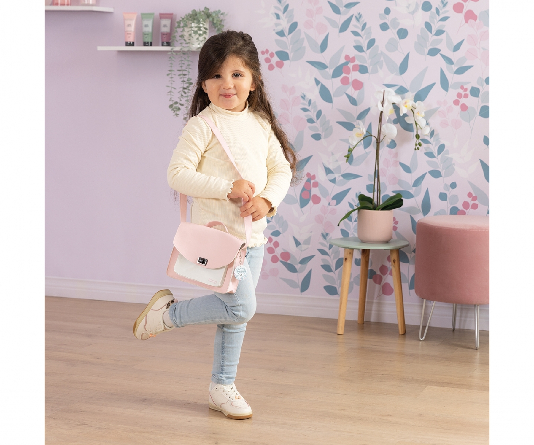 Una bambina con dolcevita color crema e jeans indossa una borsa rosa e posa.