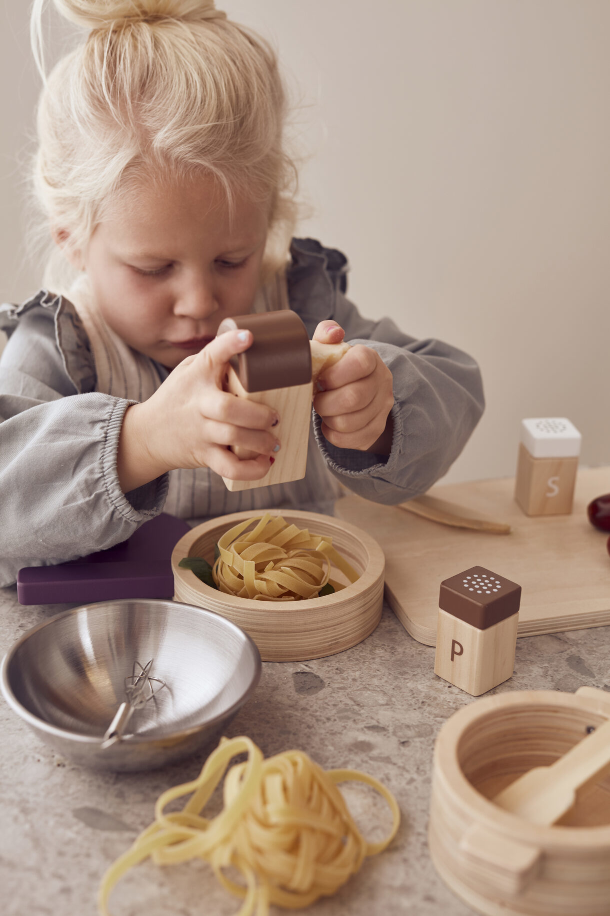 Ein kleines Mädchen mit blonden Haaren spielt mit Holzspielzeug-Nudeln.