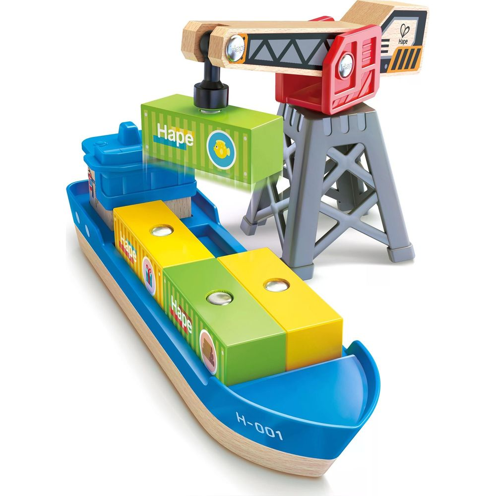 Una gru giocattolo di legno carica un container verde su una nave blu con container gialli e verdi.
