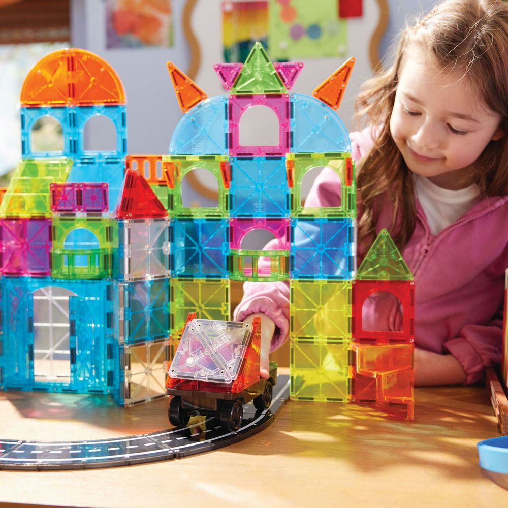 Une fille construit un château avec des blocs magnétiques colorés. Un petit camion est sur des rails.