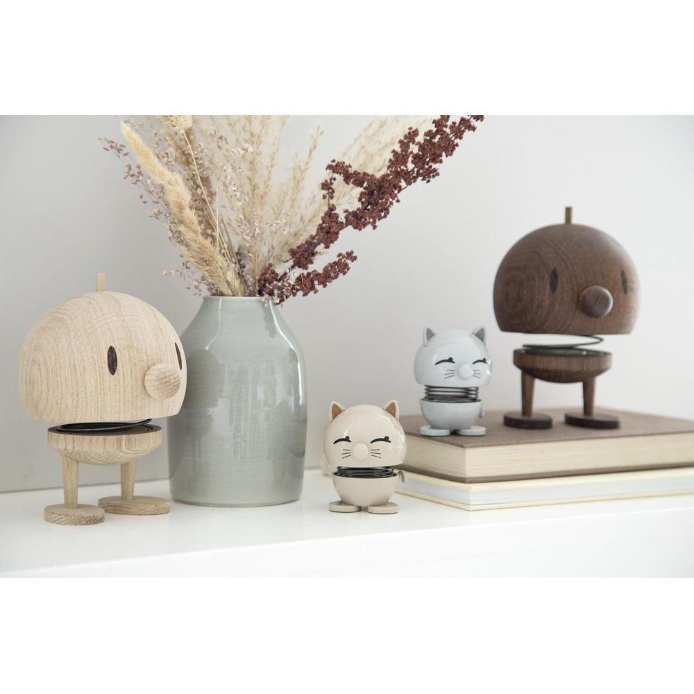 Tre figure su uno scaffale: un robot di legno, due gatti e un vaso con fiori secchi.