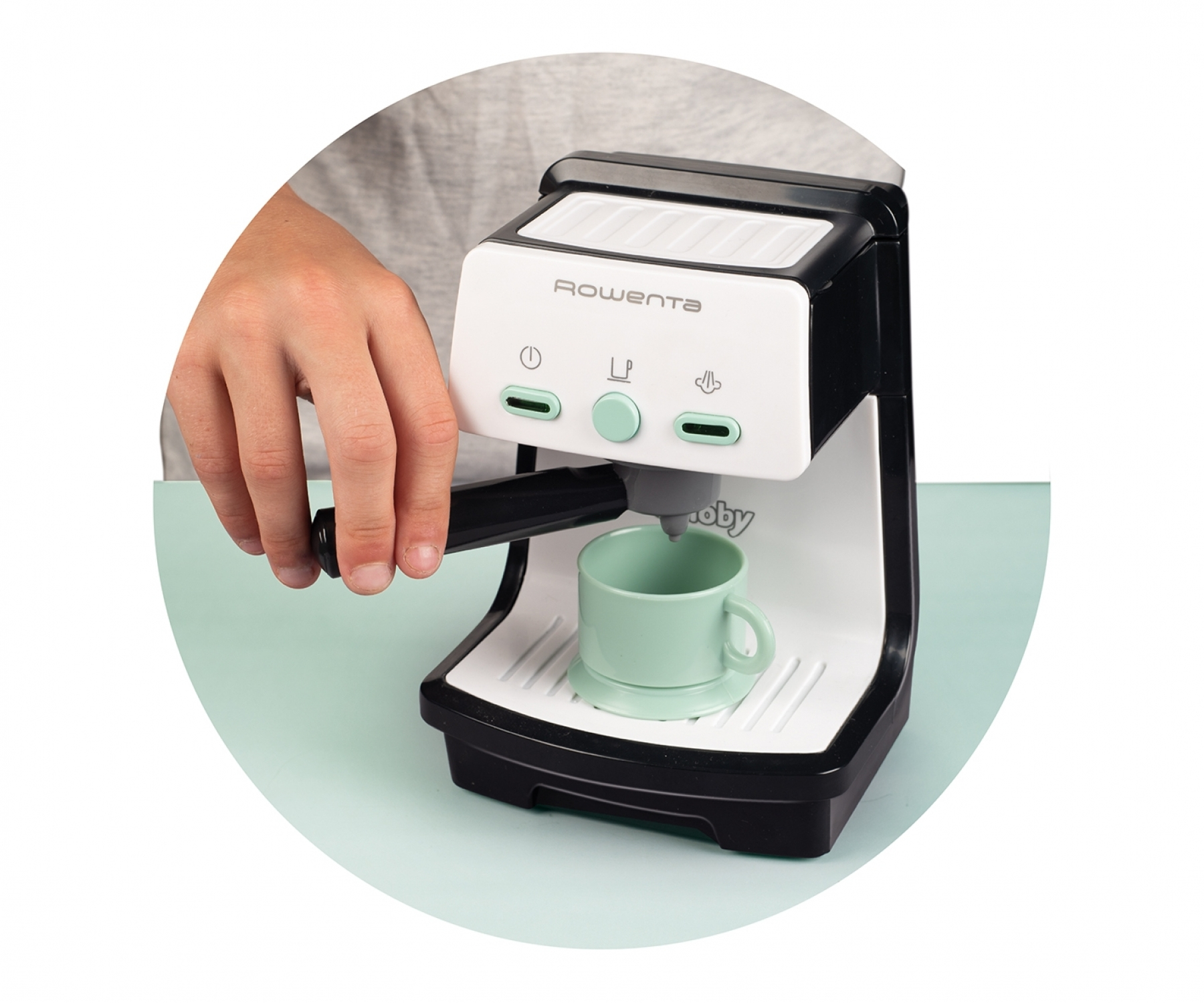 Kind benutzt eine Spielzeug-Kaffeemaschine, um eine grüne Tasse zu füllen.
