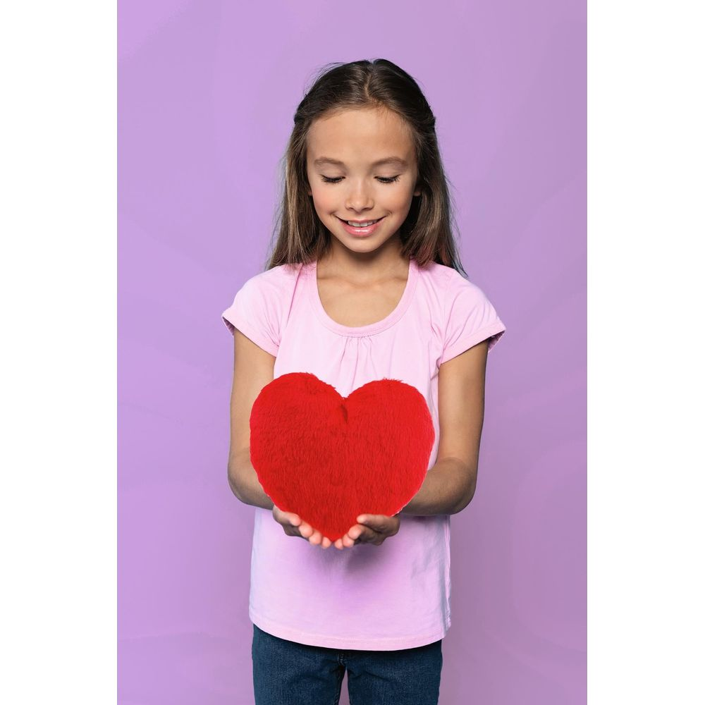 Una ragazza tiene un cuscino rosso a forma di cuore su sfondo viola.