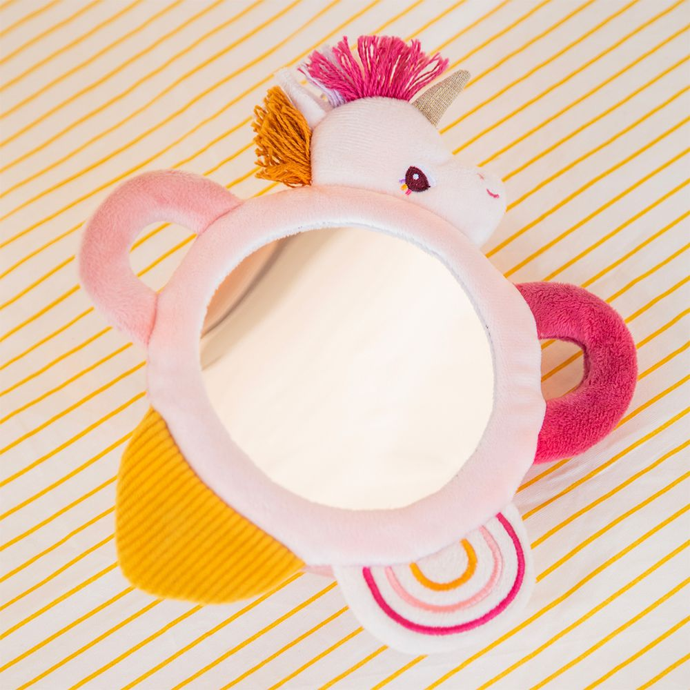 Ein rosa Einhorn-Spielzeug mit Spiegel und Regenbogen-Detail auf gestreiftem Hintergrund.