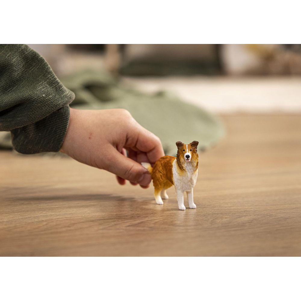 La main d'un enfant tient une petite figurine de chien marron et blanc sur un plancher en bois.