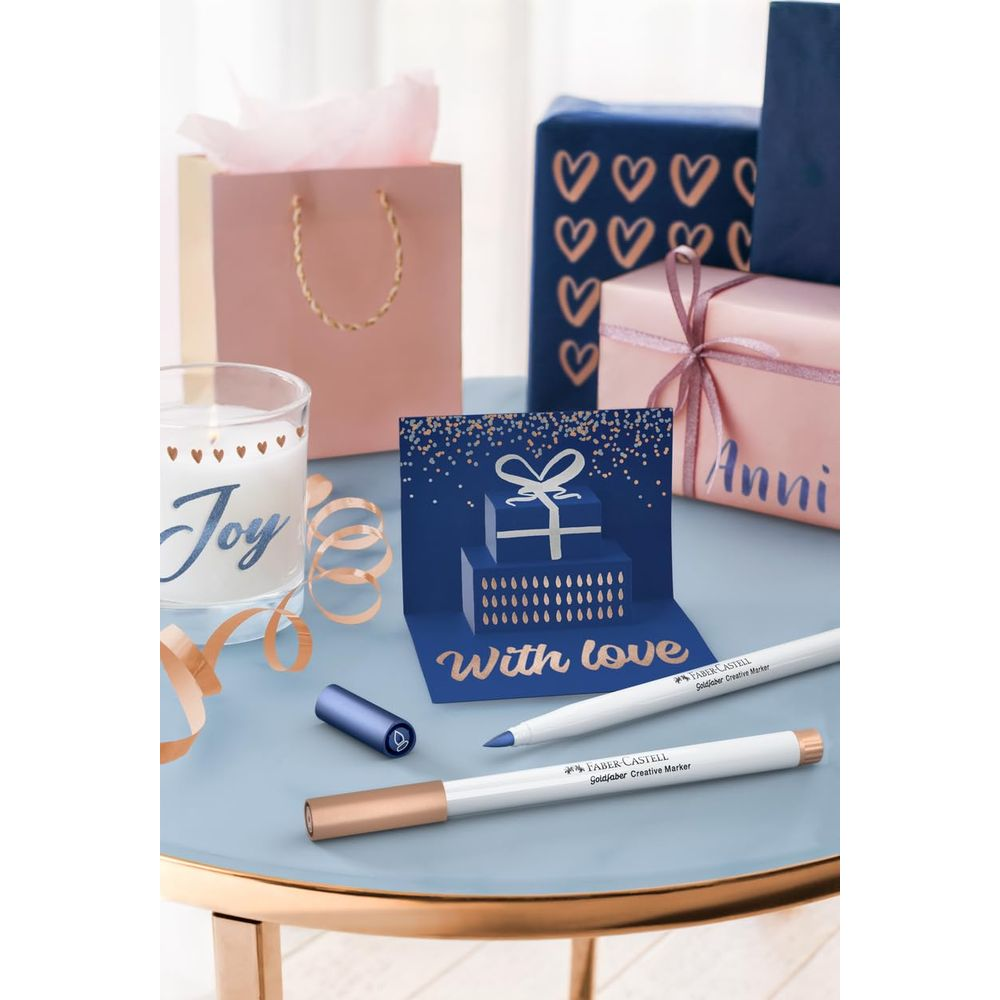 Eine blaue Pop-up-Karte mit Geschenk, neben Kerze, Geschenken und Markern.