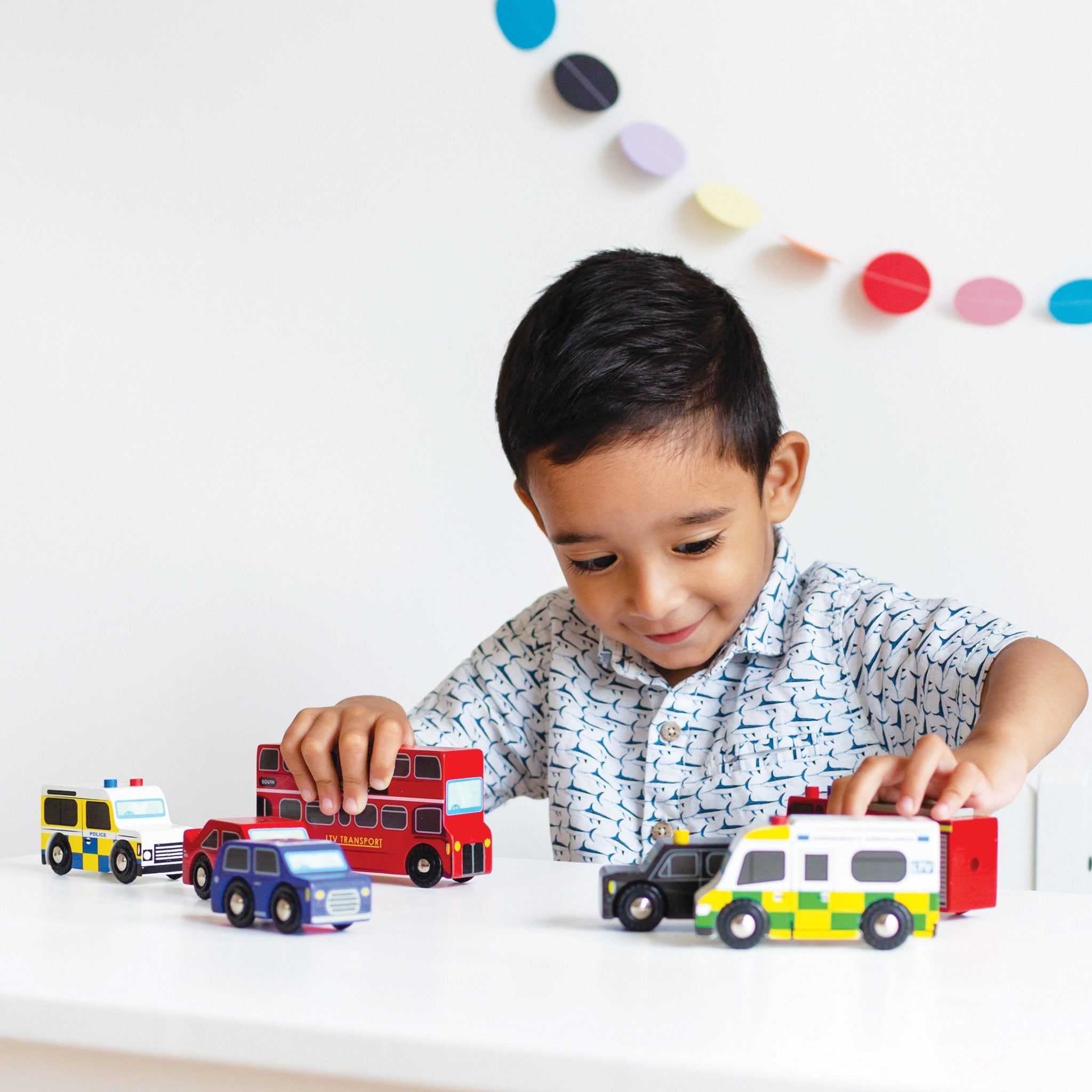 Un bambino gioca con veicoli giocattolo: ambulanza, polizia, bus, taxi.