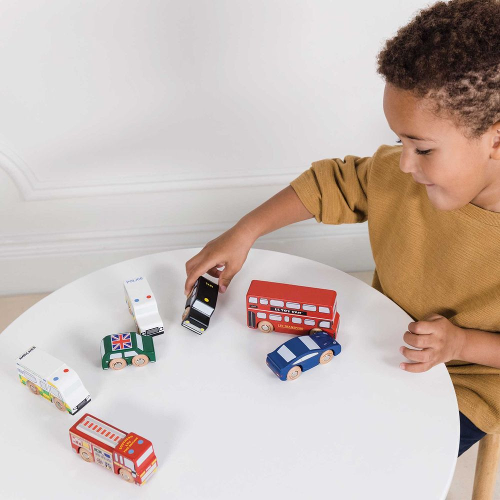 Un bambino gioca con veicoli giocattolo in legno: ambulanza, polizia, taxi, autobus, auto.