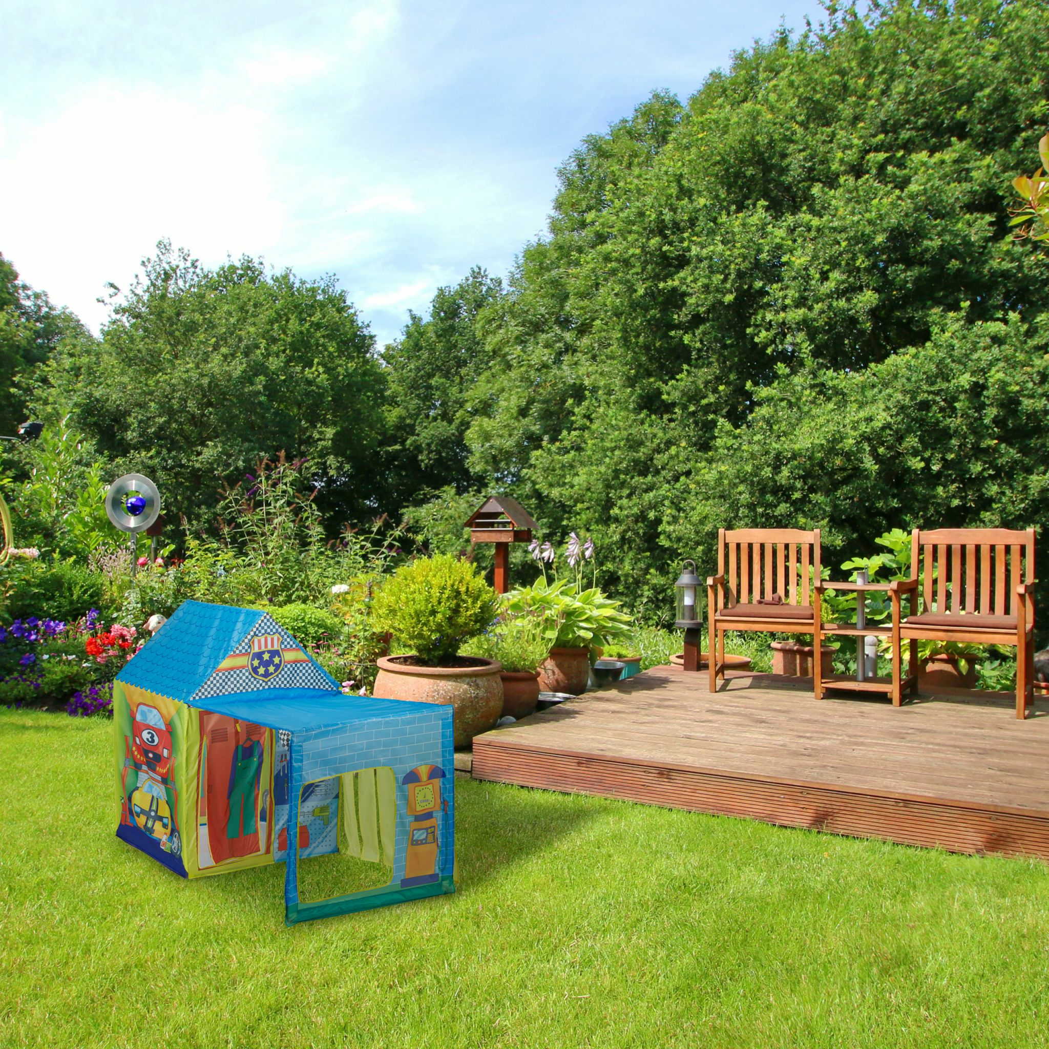 Ein buntes Spielzelt mit Auto-Motiv steht auf einem grünen Rasen neben einer Holzterrasse mit Gartenmöbeln.