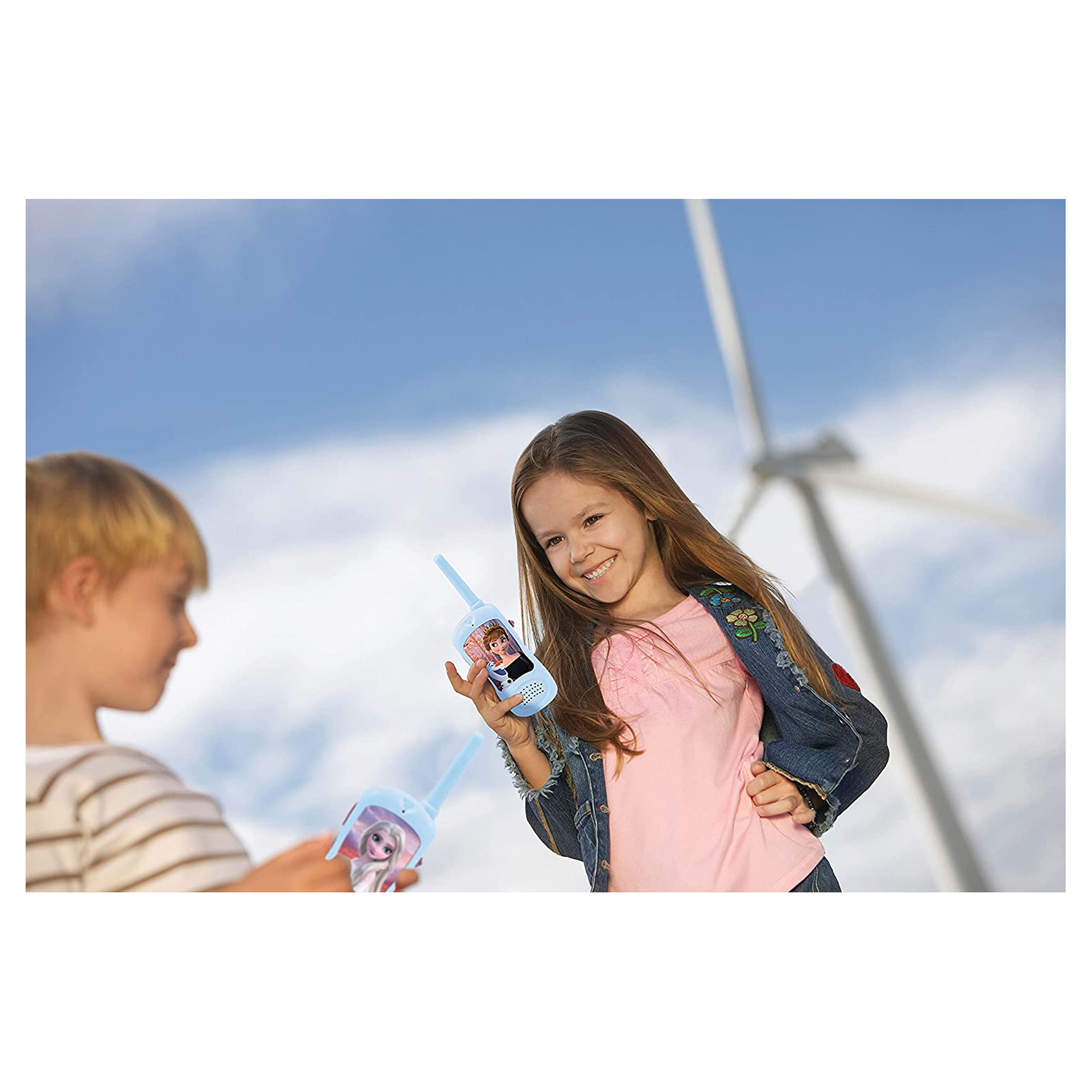 Zwei Kinder mit Walkie-Talkies vor einem Windrad unter blauem Himmel.