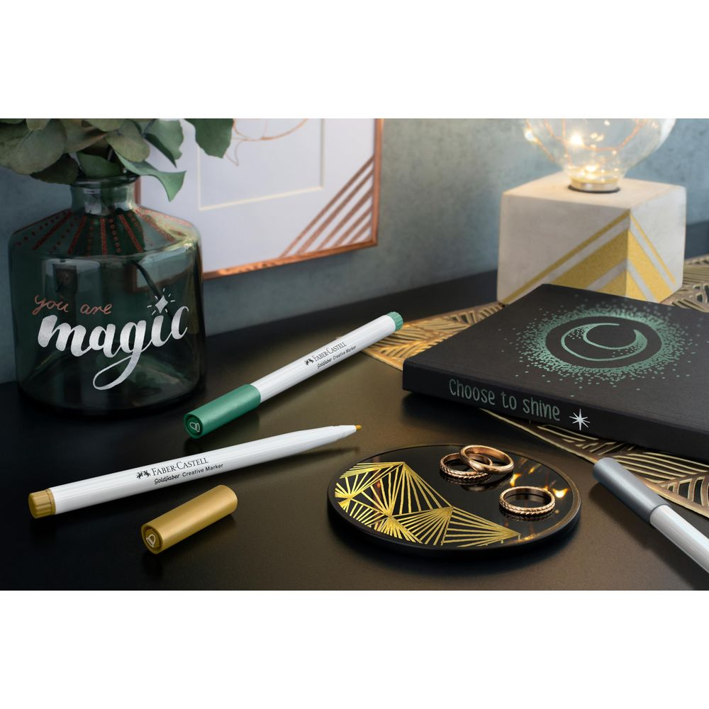 Grüner und goldener Stift auf einem Schreibtisch mit Vase und Buch.