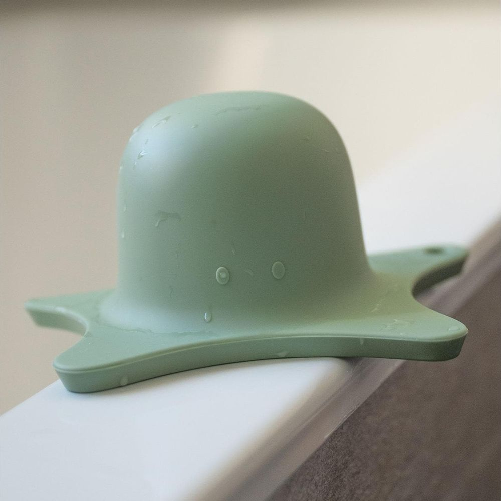 Un giocattolo da bagno verde a forma di polpo con ventose è sul bordo di una vasca da bagno.