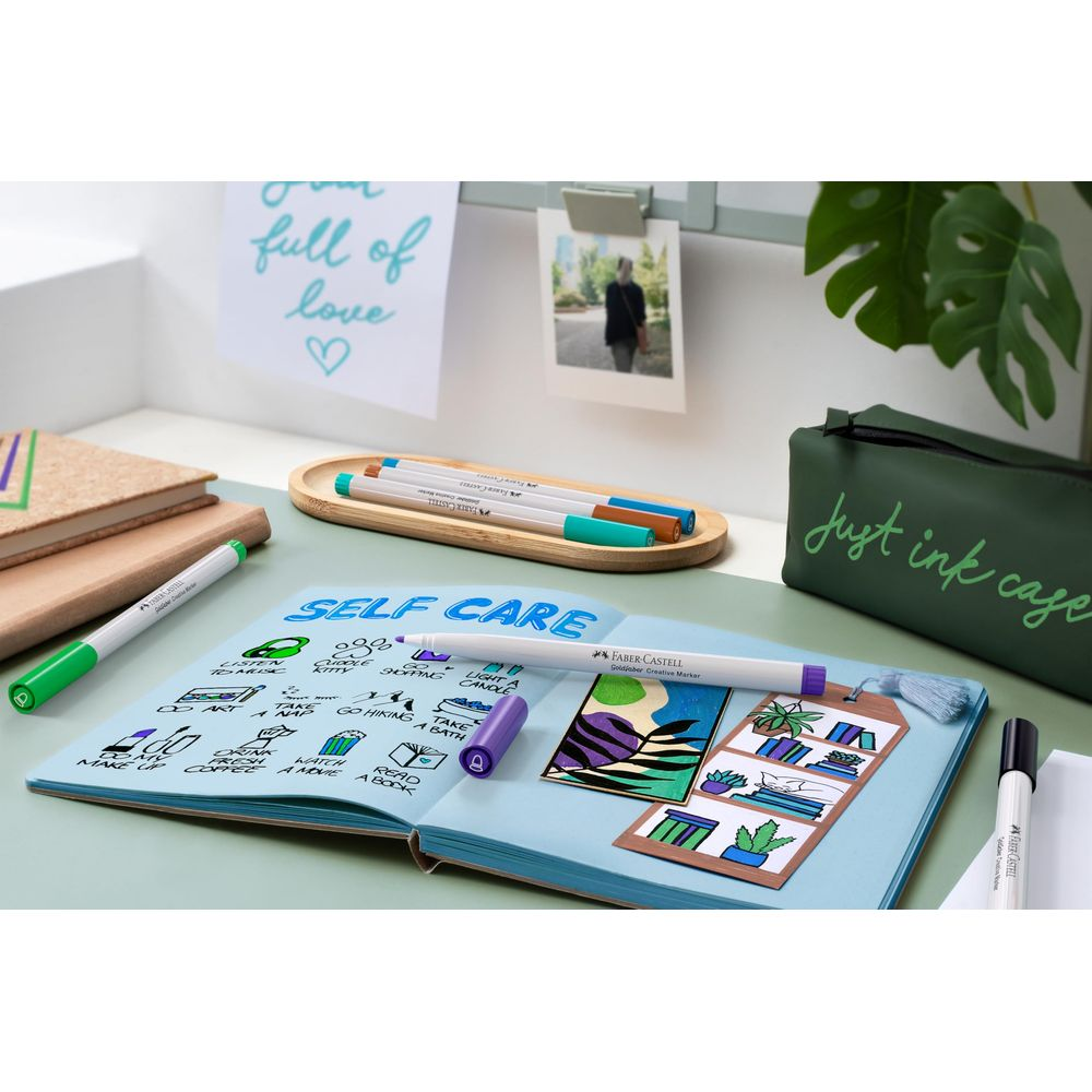 Ein offenes Notizbuch mit dem Titel „Self Care“ und Markern auf einem Schreibtisch.