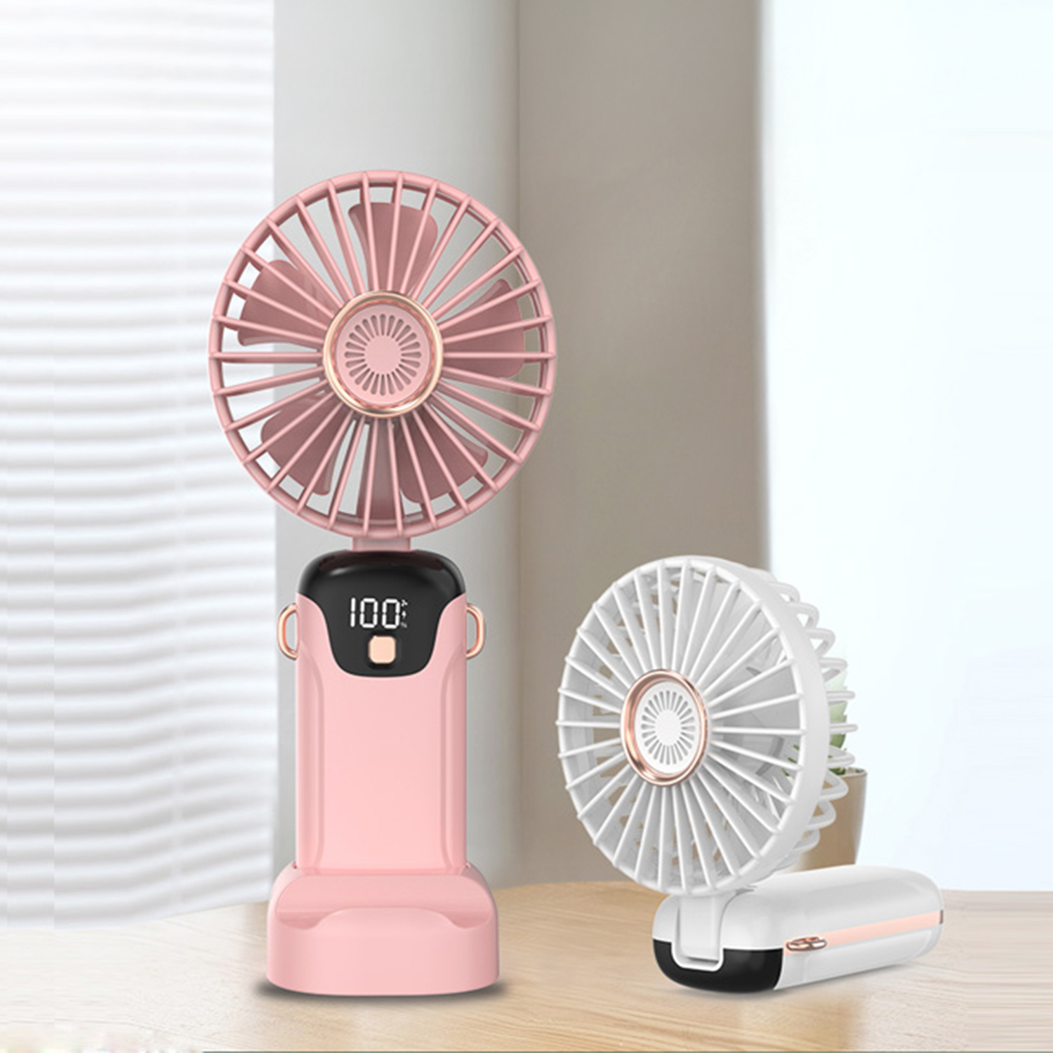 Due ventilatori portatili, uno rosa con display, uno bianco, su un tavolo di legno.
