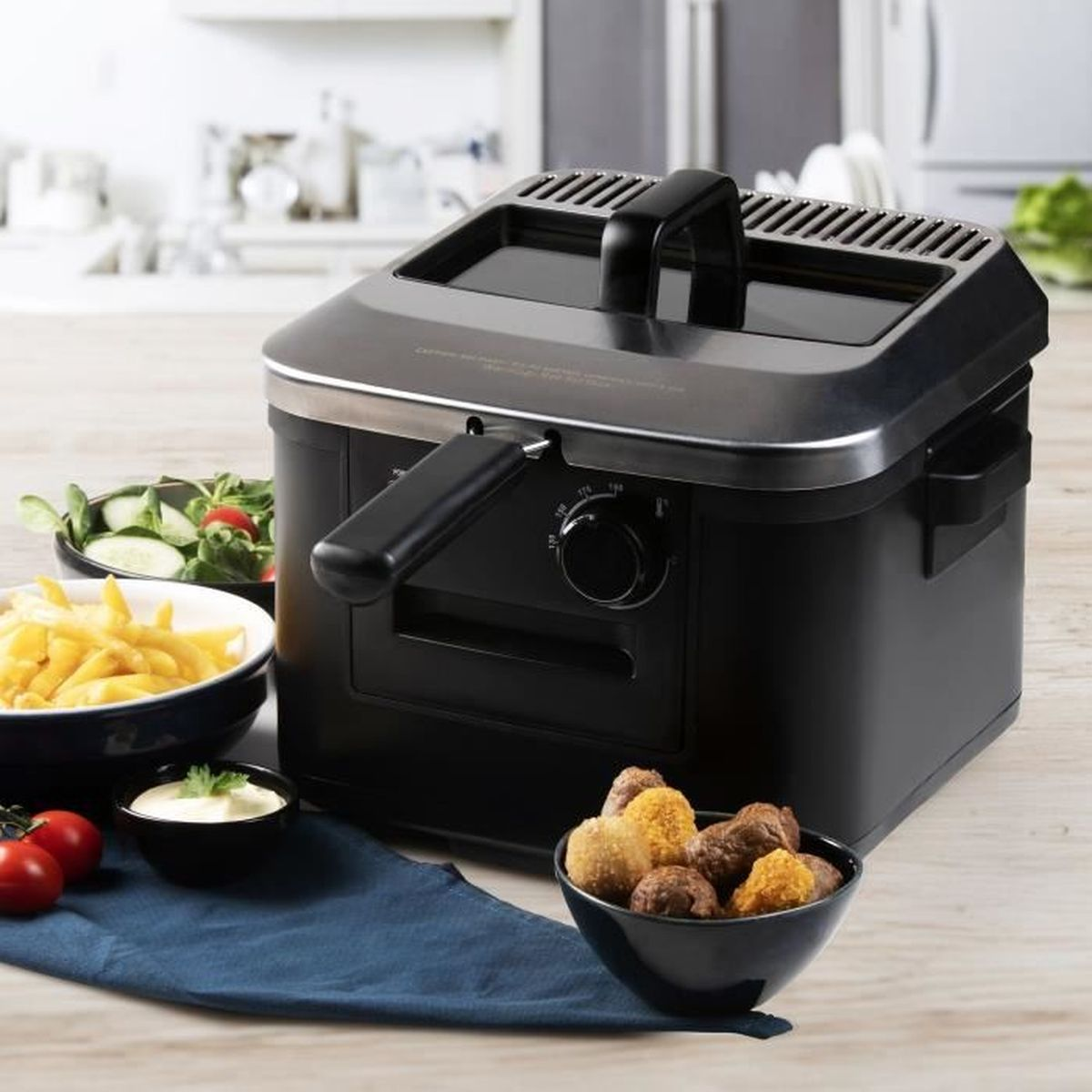 Friggitrice ad aria nera con patatine, insalata, salsa e crocchette su tavolo legno.