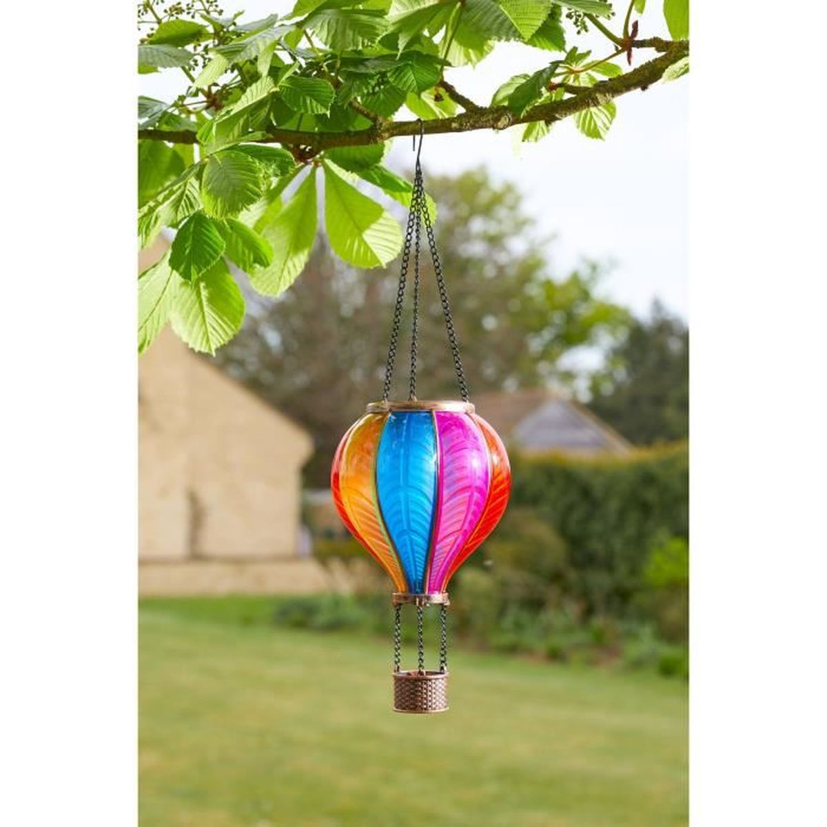 Ein bunter Heißluftballon-Anhänger mit Korbfach hängt an einem Ast über einem Garten.