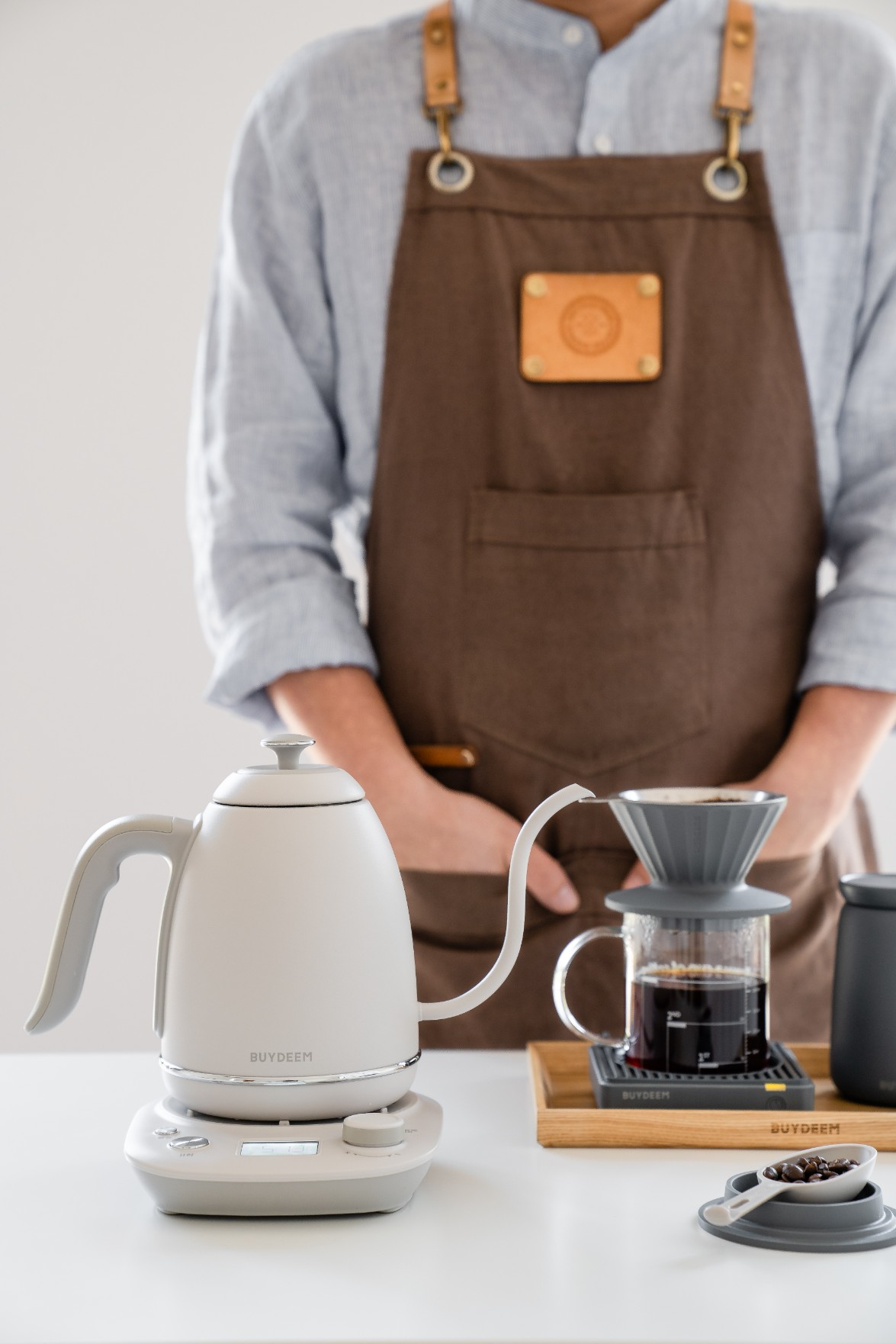 Osoba w fartuchu przygotowuje kawę metodą przelewową, z czajnikiem i ziarnami.