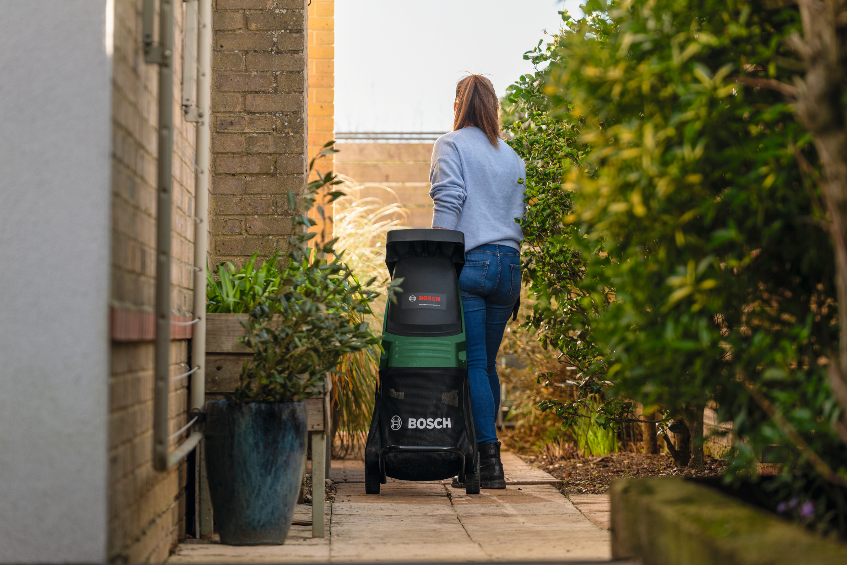 Una donna è accanto a un trituratore Bosch su un sentiero del giardino.