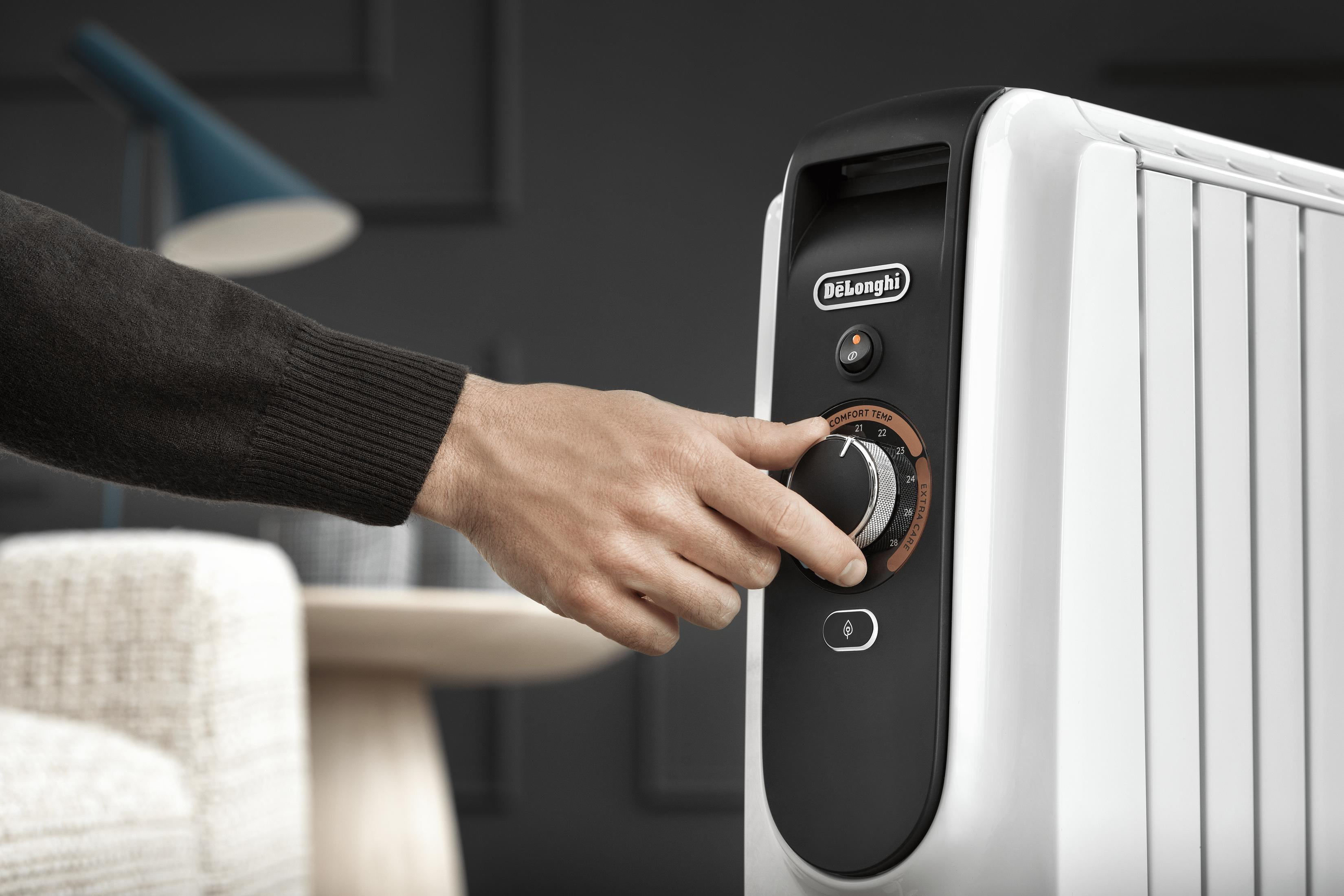 Eine Hand stellt den Thermostat eines weißen DeLonghi Heizgeräts ein.