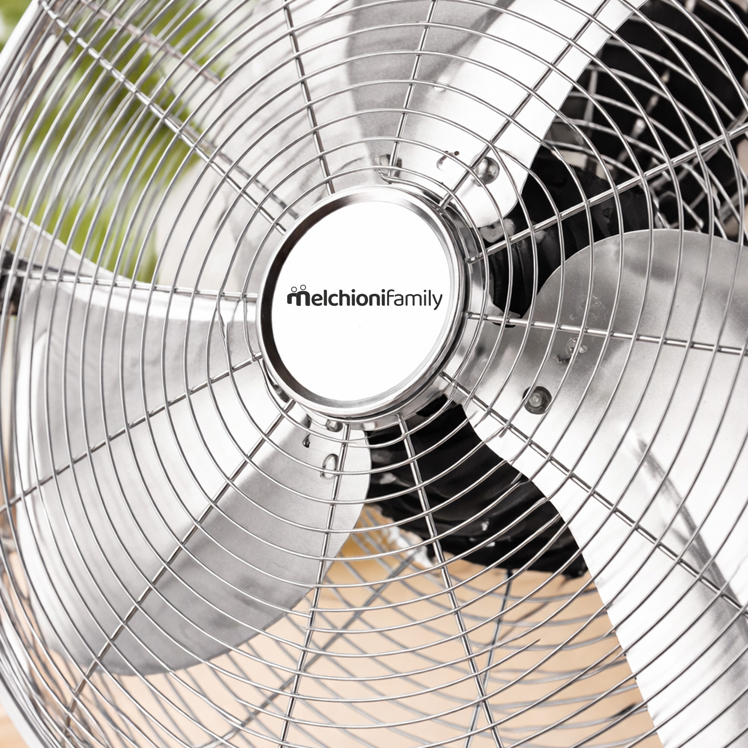 Un ventilador plateado con rejillas y aspas metálicas. Logo en el centro.