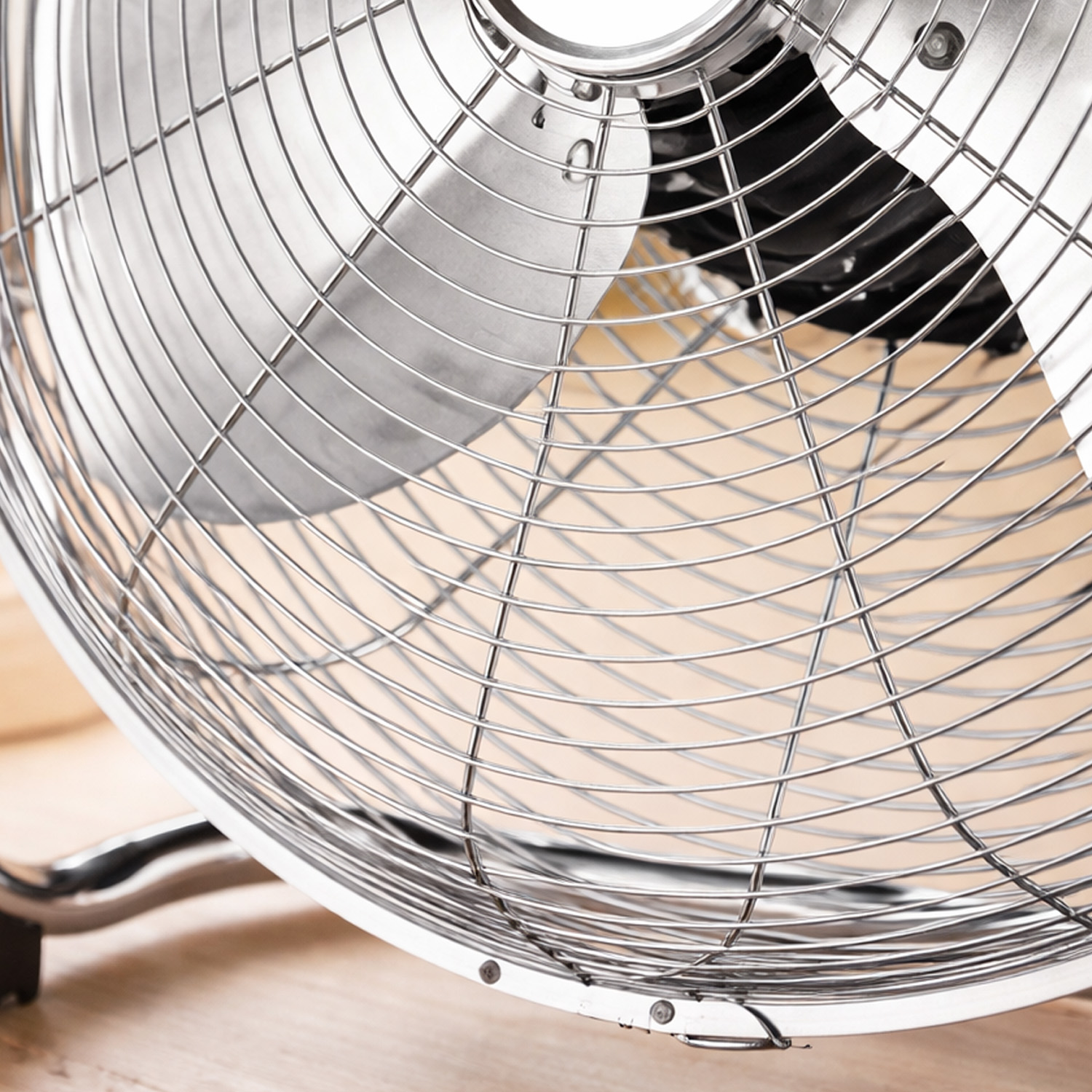 Primer plano de un ventilador plateado con rejilla metálica y aspas negras, sobre fondo de madera.