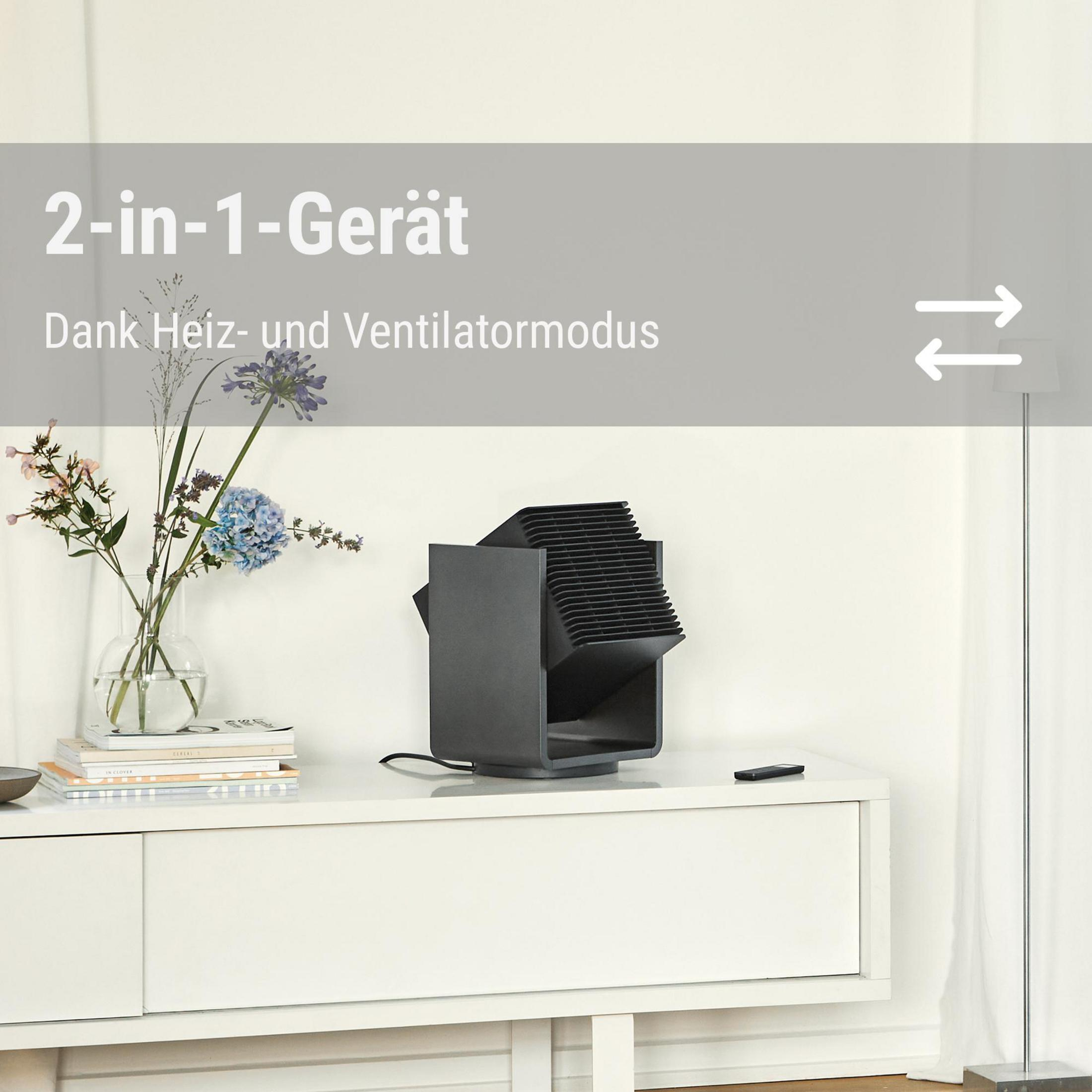 Un riscaldatore e ventilatore nero 2 in 1 si trova su una credenza bianca con fiori e libri.
